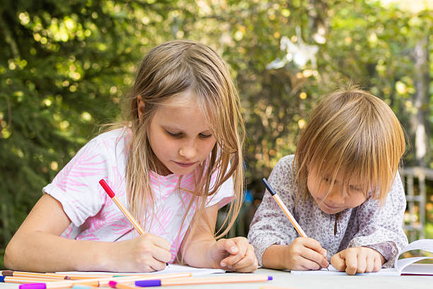 istock Two sisters drawing with fineliners in notebooks at a table in a summer garden 2207923865