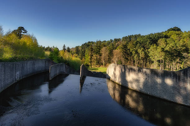 A serene scene features tranquil water way reflecting trees and a striking concrete structure, blending nature with modern architecture for all to enjoy, Bohernabreena Reservoir, Dublin, Ireland