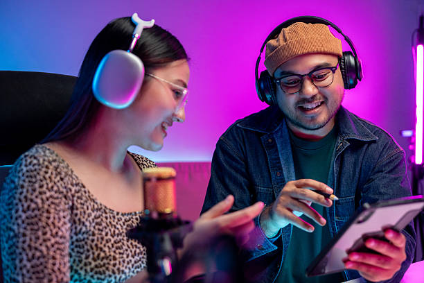 istock Young asian man and woman host streaming podcast with condenser microphone work on tablet at home broadcast studio. Content creator blogger recording voice over radio interview guest conversation 2207931598