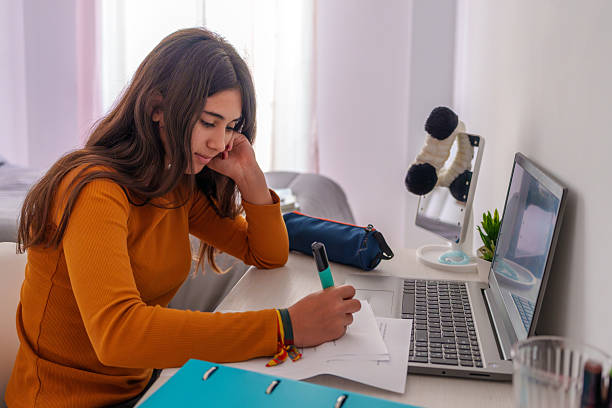 Teenage girl doing homework at home using laptop and taking notes