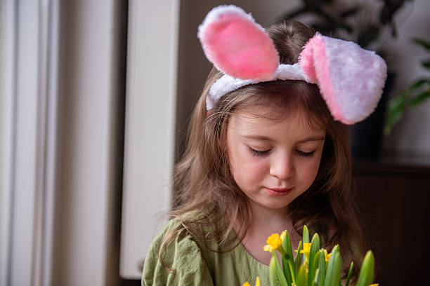 istock Little girl wearing Easter bunny ears headband looking at yellow daffodils 2207938849