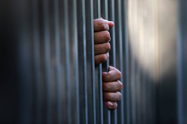 istock Hand Gripping Steel Bars of Prison Cell Symbolizing Confinement 2207940532