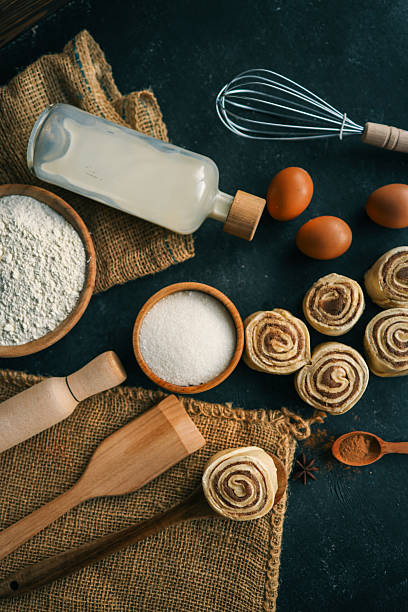 istock A top-down view of cinnamon buns on a dark surface with flour, sugar, eggs, milk, and a rolling pin, perfect for baking and recipe themes. 2207948175