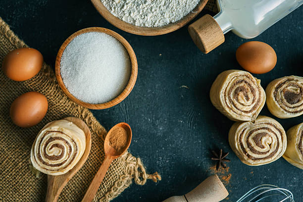 istock A top-down view of cinnamon buns on a dark surface with flour, sugar, eggs, milk, and a rolling pin, perfect for baking and recipe themes. 2207948194