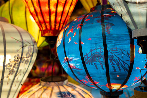 Vibrant, intricately patterned lanterns in assorted shapes and colors hang gracefully along a timeworn Vietnam market, showcasing exquisite traditional artistry.
