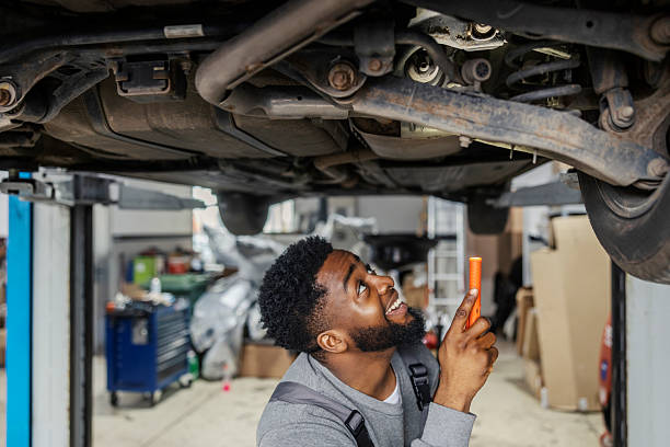 istock Multicultural auto mechanic standing under chassis at auto repair shop and looking for malfunction with his lamp. 2207955650