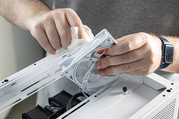 istock Technician wiping dust from white computer cooling fan removed from top panel of PC case during maintenance or system cleaning process 2207956111