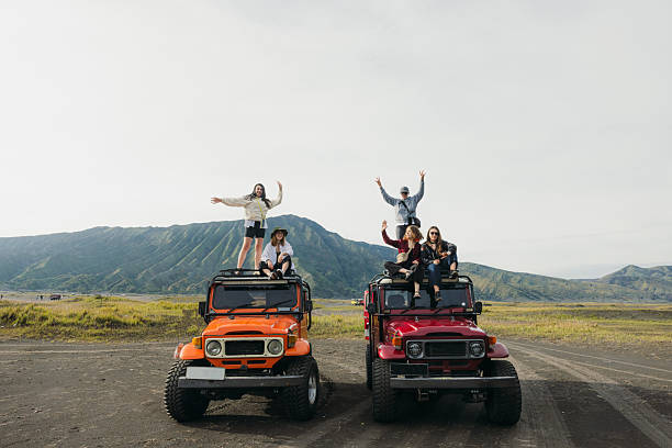 Group of five happy female friends on top of red jeep overlooking dramatic volcanic landscape of Bromo Tengger Semeru National Park, East Java island
