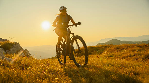 istock Woman Mountain Biking Uphill through Open Fields at Golden Hour 2207965098