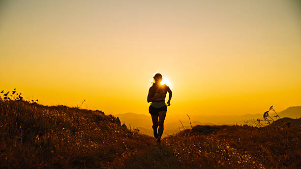 Woman Runs along a Grassy Mountain Trail,Silhouetted by the Bright Setting Sun Behind Her. The Image Captures her Dynamic Motion and Determination in the Beautiful,Challenging Mountain Environment During the Golden Hour