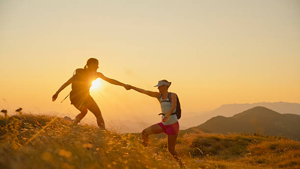 istock Women Helping Each Other Hike Up Mountain Slope at Sunset 2207965244