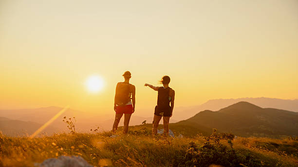 istock Two Women on Mountain Ridge Pointing at Sweeping Sunset View 2207965249