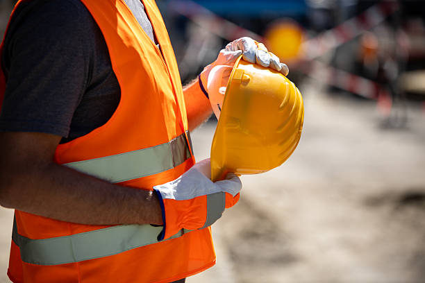 istock Worker in safety gear holds yellow hard hat at construction site during daylight hours 2207965763
