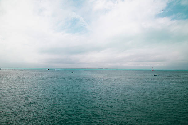 Small boats navigating the vast ocean under a cloudy sky