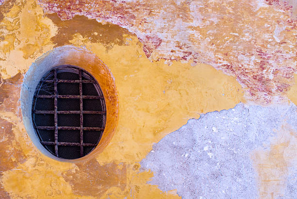 Small oval barred window in a weathered painted wall.