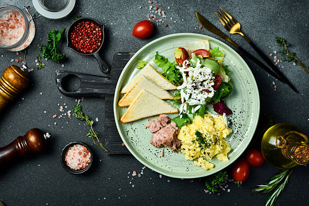 istock Breakfast. Plate with scrambled eggs, tuna, salad and toast bread. On a black stone background. Free space for text. 2207975186