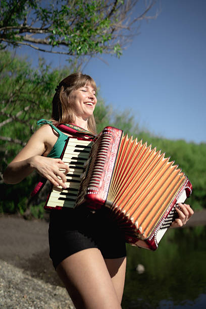 istock Young woman playing accordion outdoors by the river 2207976420