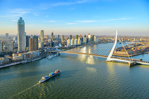 Rotterdam sunset view of the skyline seen from a height at the New Maas with a container ship passing the Erasmusbrug and the Zalmhaven. The bridge, often referred to as the \