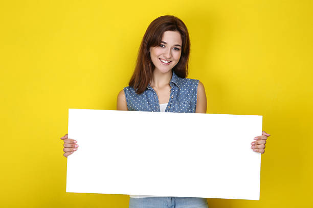 istock Young woman with blank board on yellow background 2207980103