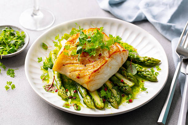 Fried cod with asparagus and on plate. Grey background. Close up.