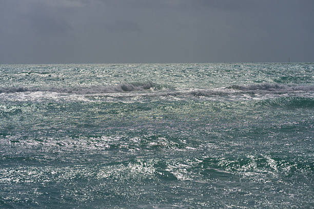 A serene seascape featuring turquoise ocean waves crashing on a beach under a dramatic overcast sky. Captures the natural power and beauty of the coastline during an impending storm.