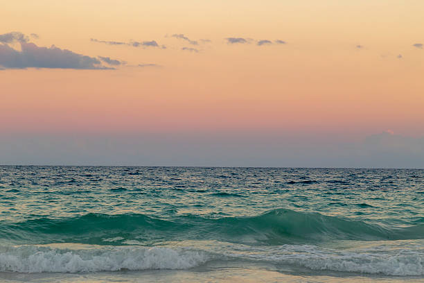 Calm turquoise ocean waves gently washing onto the sandy beach as the sun sets, painting the sky with vibrant hues of pink and orange in tulum, mexico