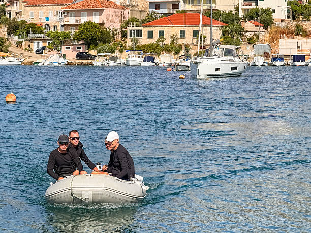 A group of 4 sailors navigates a dinghy back to their sailboat, floating on calm waters. The crew approaches the yacht after an excursion, embodying the adventure and freedom of the sailing lifestyle. Perfect for themes of maritime travel, yachting, and nautical vacation.