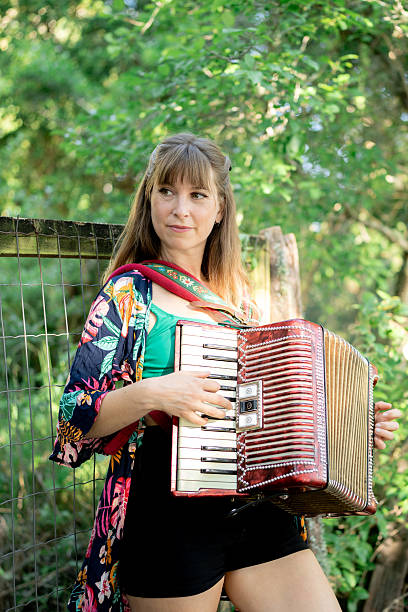 Young woman musician playing the accordion in a lush garden, surrounded by vibrant trees and enjoying a sunny day filled with joy