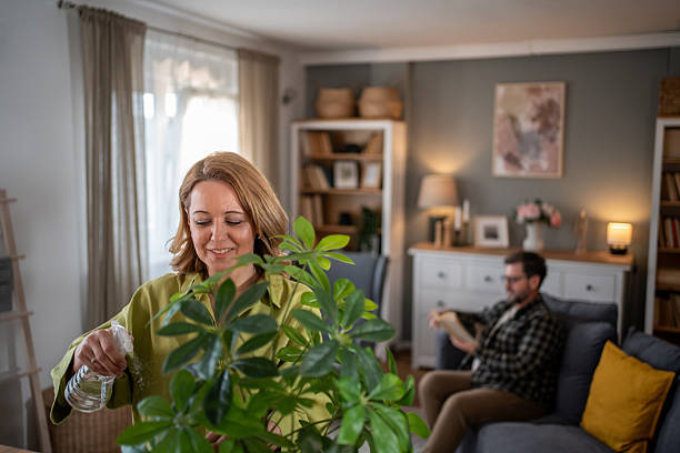 istock Woman watering plants while man reading on sofa in living room 2208009365