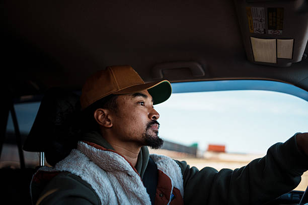 Profile view of a handsome Filipino man in his 30s driving his car on a sunny day in San Francisco, California.