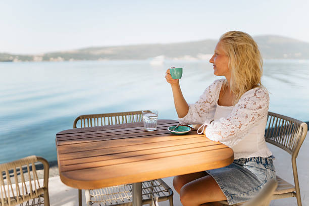 istock Young blond woman drinking coffee in a seaside cafe 2208012440