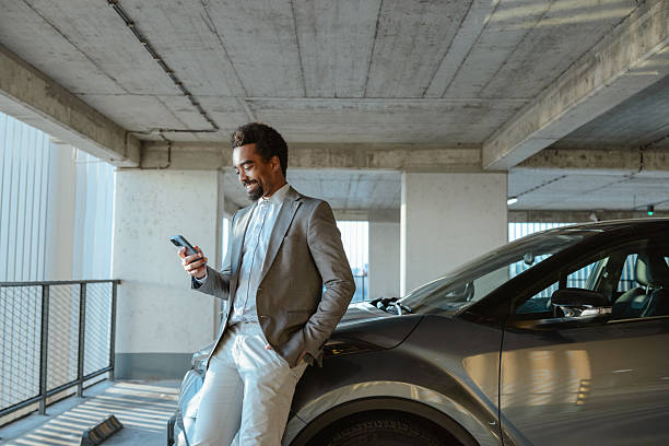 istock Businessman leaning on car in parking lot using smartphone 2208012584