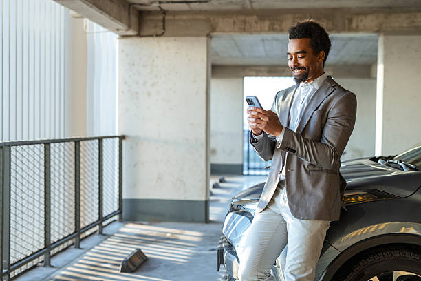 istock Businessman texting on smartphone while leaning on car in urban parking area 2208013641
