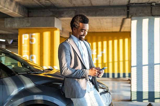 istock Man standing by parked car in modern parking lot using smartphone 2208013869