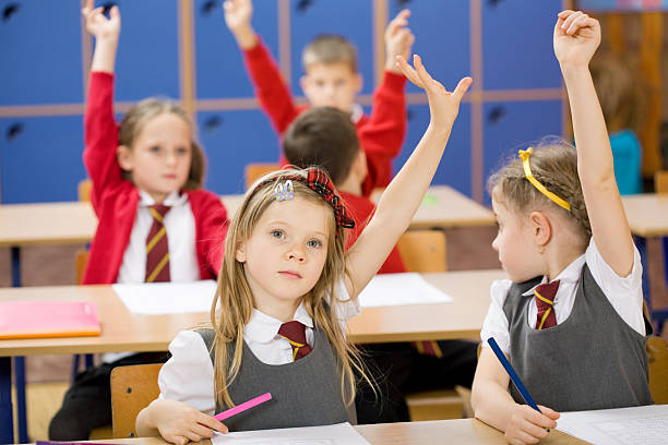 Elementary school kids raising their hands to answer a question.