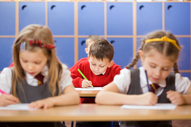istock Elementary school kids in a classroom writing. Focus on a boy in the center. 2208028192