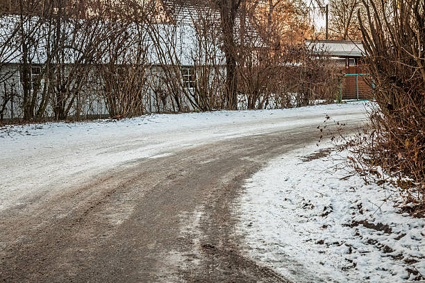 Rural countryside road in Austria, visibly covered in ice, snow, and frost, presenting a typical winter driving hazard. The photograph underscores the challenges of driving during winter, highlighting the need for cautious driving and preparation for hazardous road conditions. Ideal for illustrating winter travel safety, road hazards, driving conditions, seasonal driving in Europe, and winter landscape scenes.