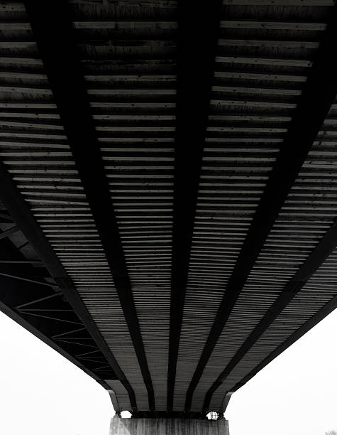 Industrial elegance captured in converging lines and shadows, where modern architecture meets geometric precision beneath and urban overpass.