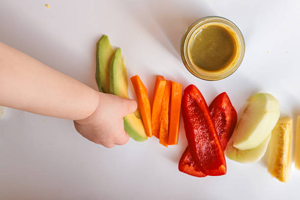 istock A child's hands reaching for freshly chopped vegetables on a white surface. Includes diced avocado, carrot, apple slices, bell pepper, and tomato pieces. Minimalist food composition. 2208051541