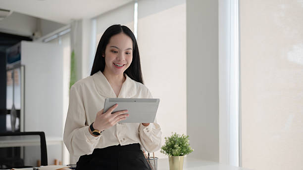 istock Female office worker is smiling and looking at a tablet while standing in front of working table. 2208053151