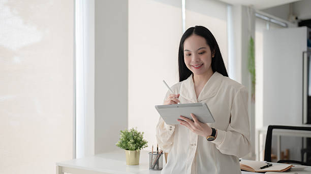 istock Female office worker is writing on tablet with stylus while standing in front of working table. 2208053166
