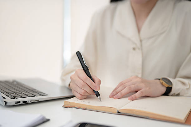 istock Office worker or clerk holding a fountain pen writing in notebook while sitting at table in office. 2208053267