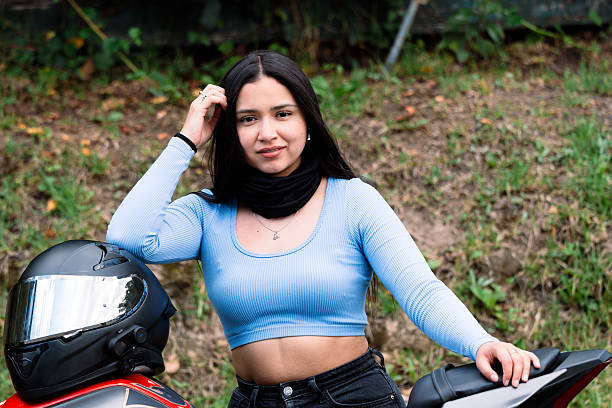 Portrait of a beautiful young woman motorcyclist smiling while posing with her stylish red motorcycle and sleek black helmet in the summer sun
