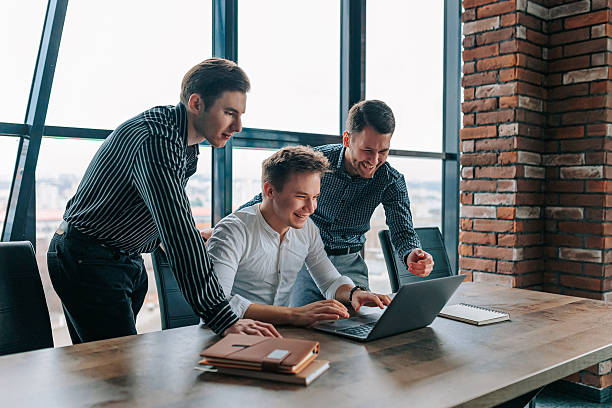istock Young businessmen celebrate project success together in modern office environment while working on laptops 2208063329