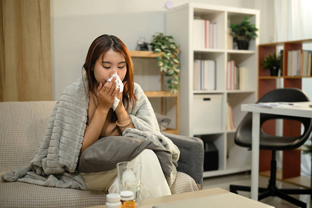 istock Young asian woman experiencing cold and flu symptoms, sneezing into a tissue. 2208069924