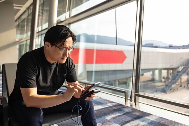istock Asian male backpacker traveling alone using mobile phone to search for information online in airport waiting area 2208073711
