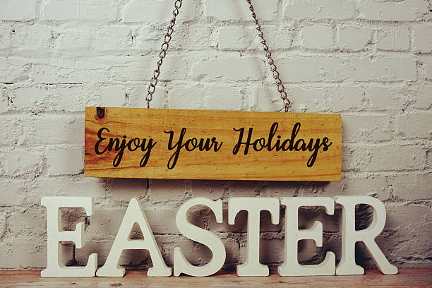 istock Happy Your Holidays Easter text with Easter alphabet letters and empty signboard hanging on white brick wall background 2208074559