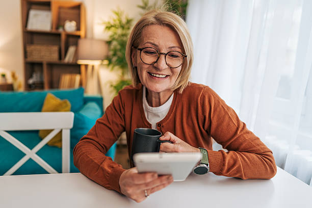 istock Smiling senior woman using digital tablet and drinking coffee at home 2208074578