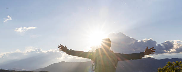 Mature man celebrates on mountain top at sunrise, arms outstretched towards sun, Liguria