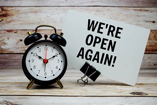 istock We're Open Again text on paper card with alarm clock on wooden background 2208077450